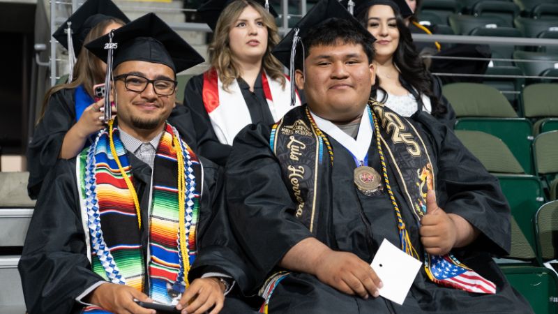 Two WVC students sitting at graduation ceremony wearing decorative stoles