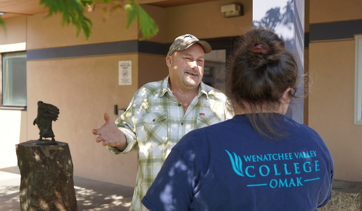 A WVC Omak senate member speaks with a woman wearing a blue WVC Omak t-shirt.