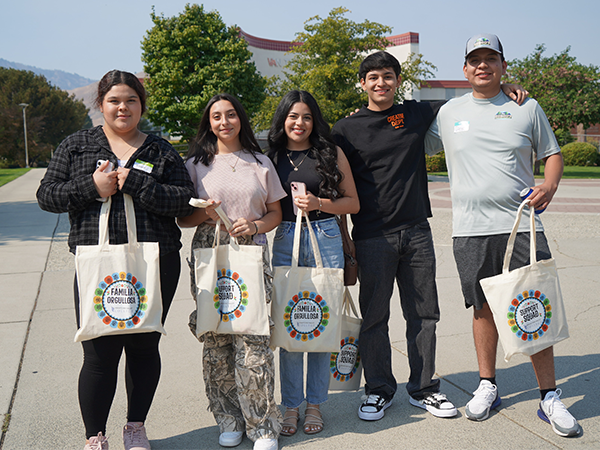 Five students stand in a group holding tote bags that they received at the new student orientation.