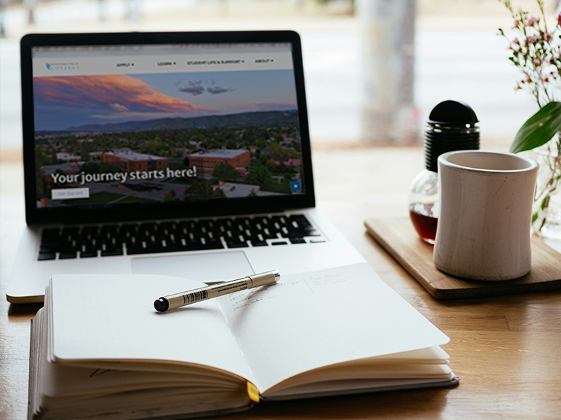 Laptop on desk with book and drink.