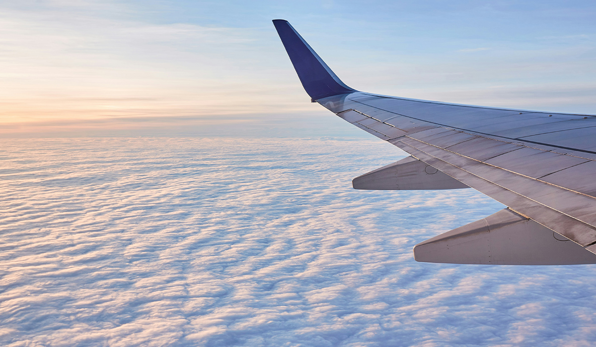 A view from an airplane window of the airplane's wing, clouds, and blue sky.