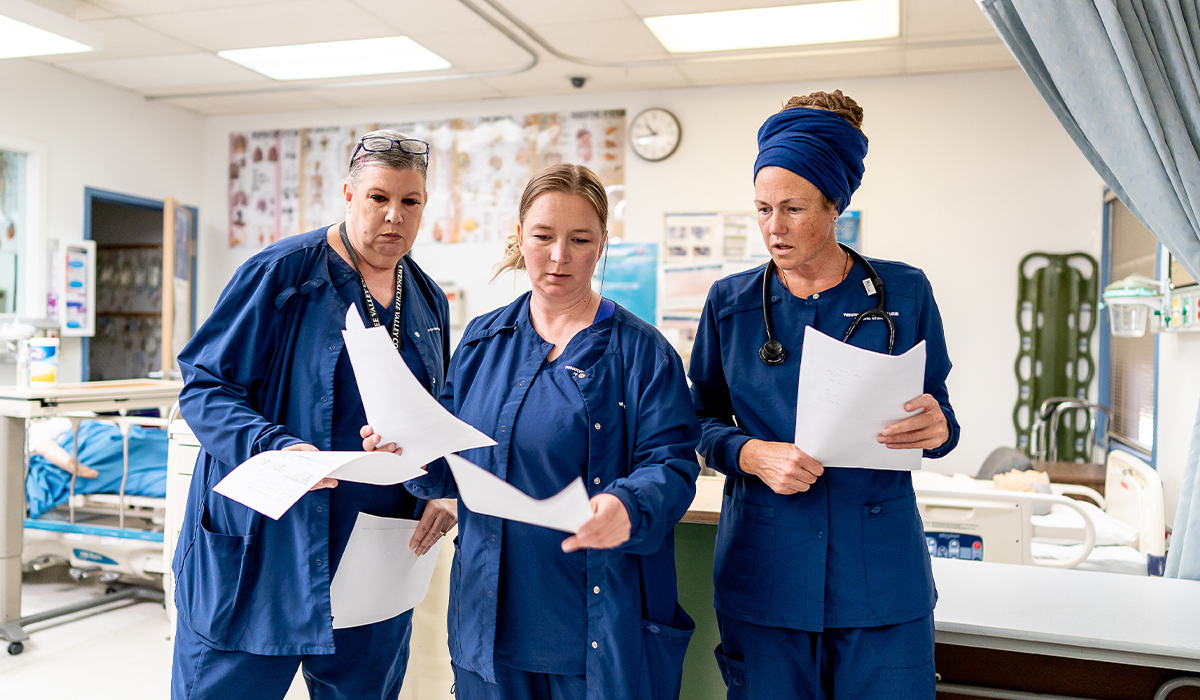 Two WVC Omak nursing students stand next to their professor in a lab and look over paperwork.