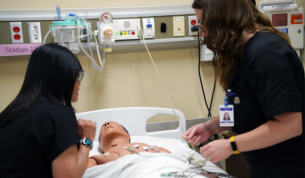 A medical assistant professor talks a student through a practice on a manikin.
