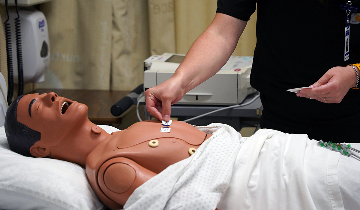 A student places heart monitoring devices on the chest of a manikin.