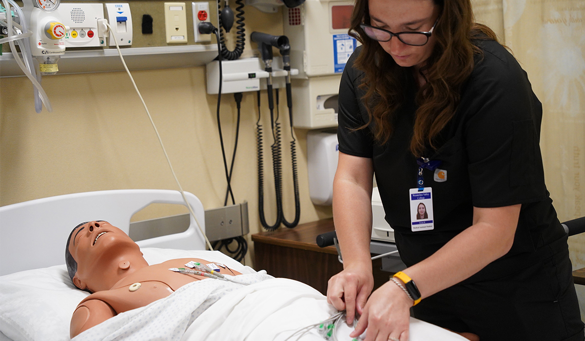 A student places heart monitoring devices on a manikin.