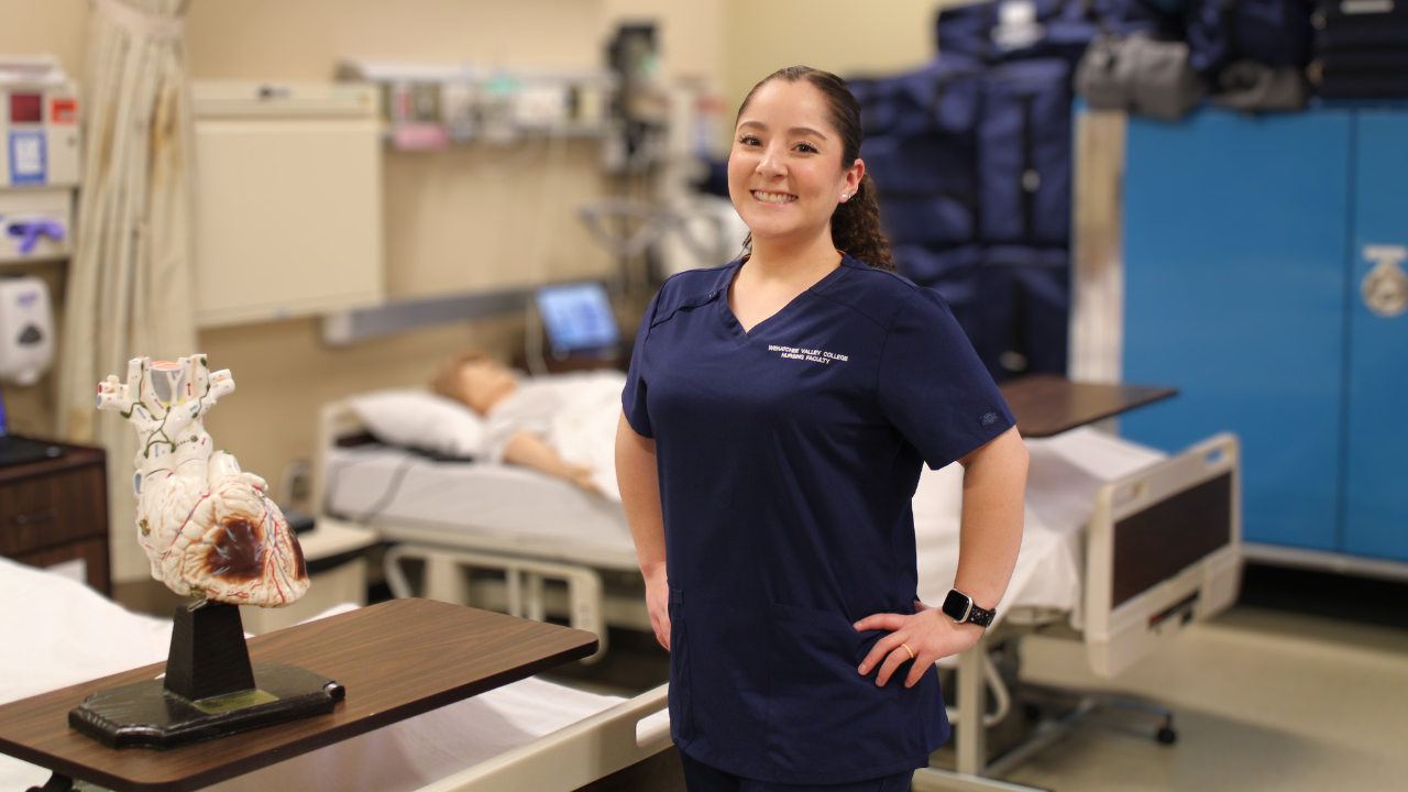 Professor Carolina Martinez Calderon stands in a nursing lab next to a hospital bed.