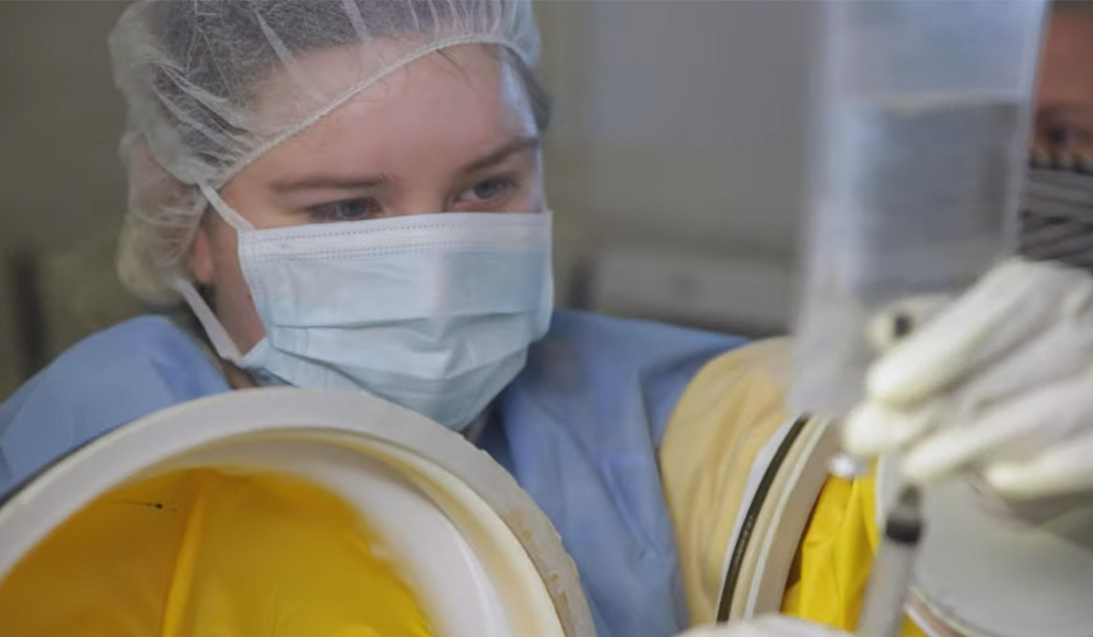 A pharmacy tech student in protective clothing works with a bottle of medicine.