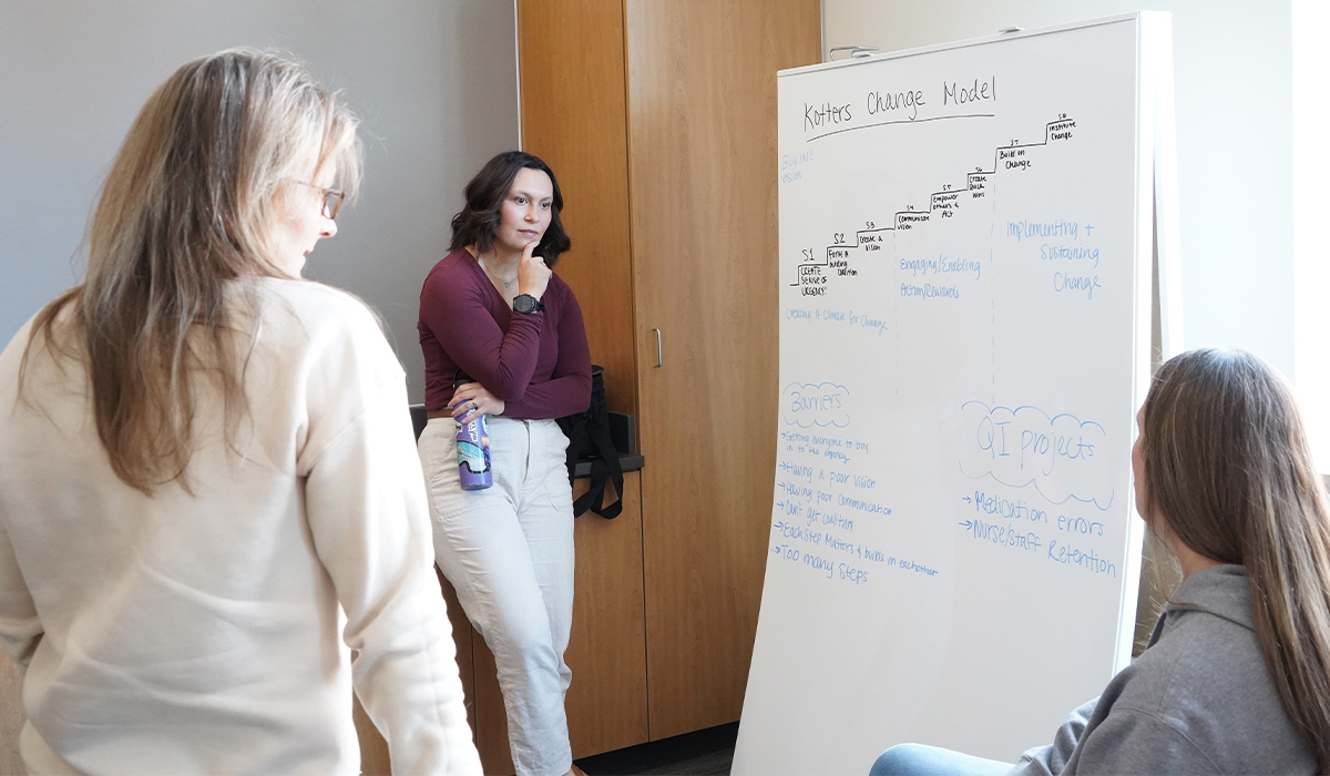 Two RN to BSN students talk with their professor about a group project.