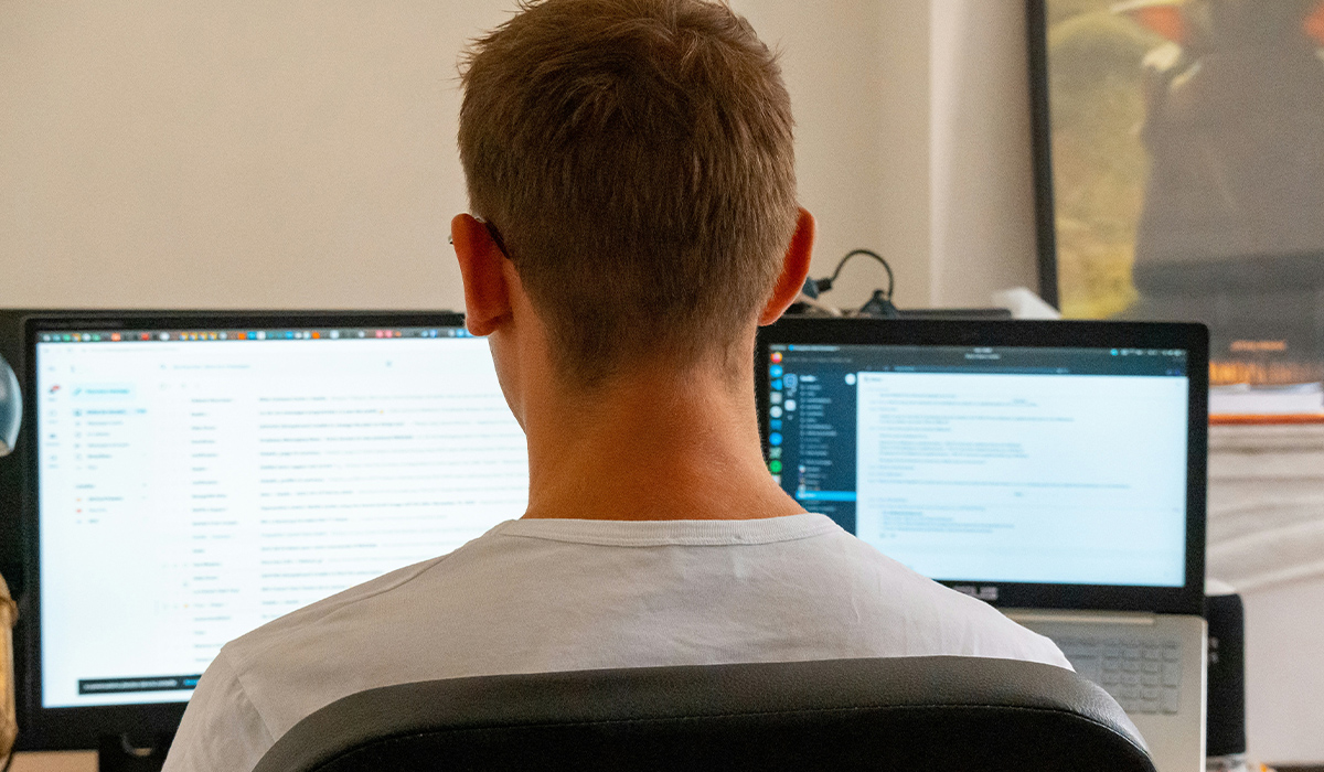 A view from behind a student sitting in a chair and looking at dual computer monitors.