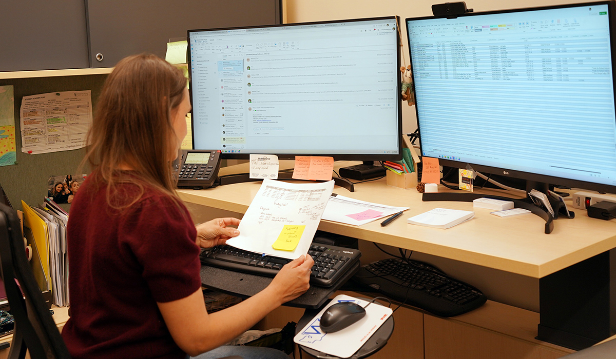 A staff member sits at a computer and works on an Excel spreadsheet.