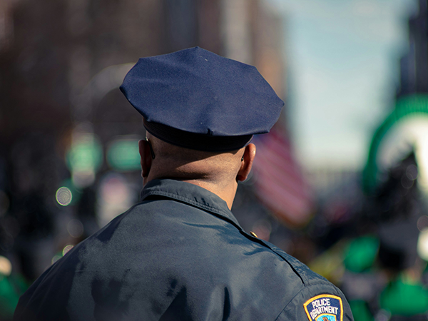 A view from behind a police officer who is wearing a dark blue coat and cap.