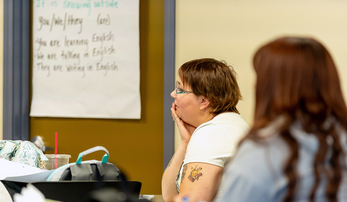 Two students sit at tables in a classroom.