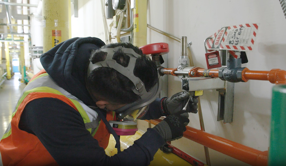 An ESRT student wearing protective equipment works on a pipe.