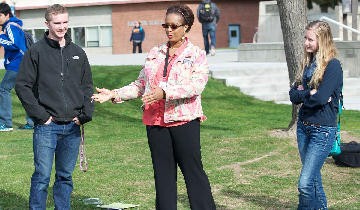 The Communications Studies professor and her students stand outside on the lawn doing an activity.