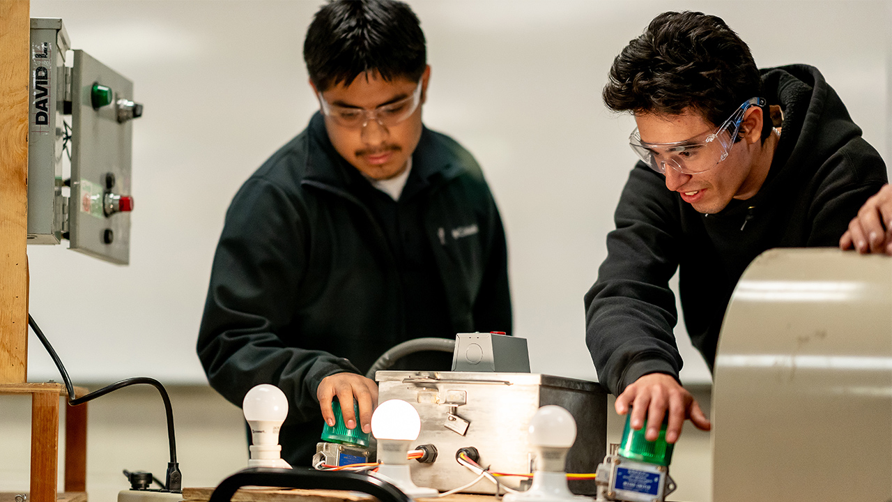 Two students demonstrate an electronics project that turns on lightbulbs.