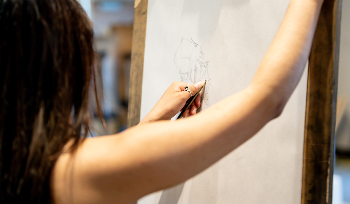 An art student stands in front of an easel and works on a sketch.