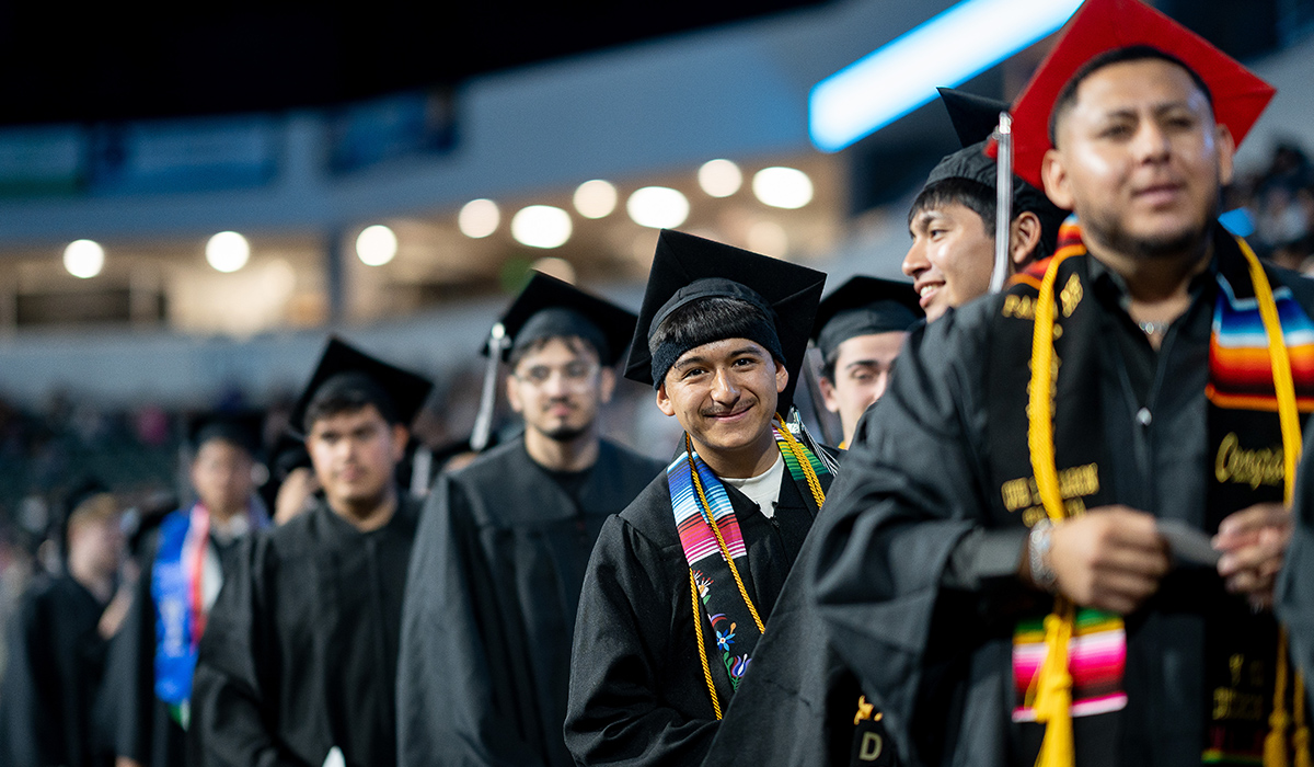 A WVC graduate standing in a long line of graduates leans out and smiles at the camera.