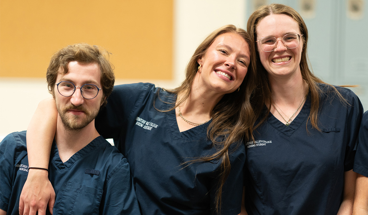 Three nursing graduates wearing dark blue scrubs smile at the camera.