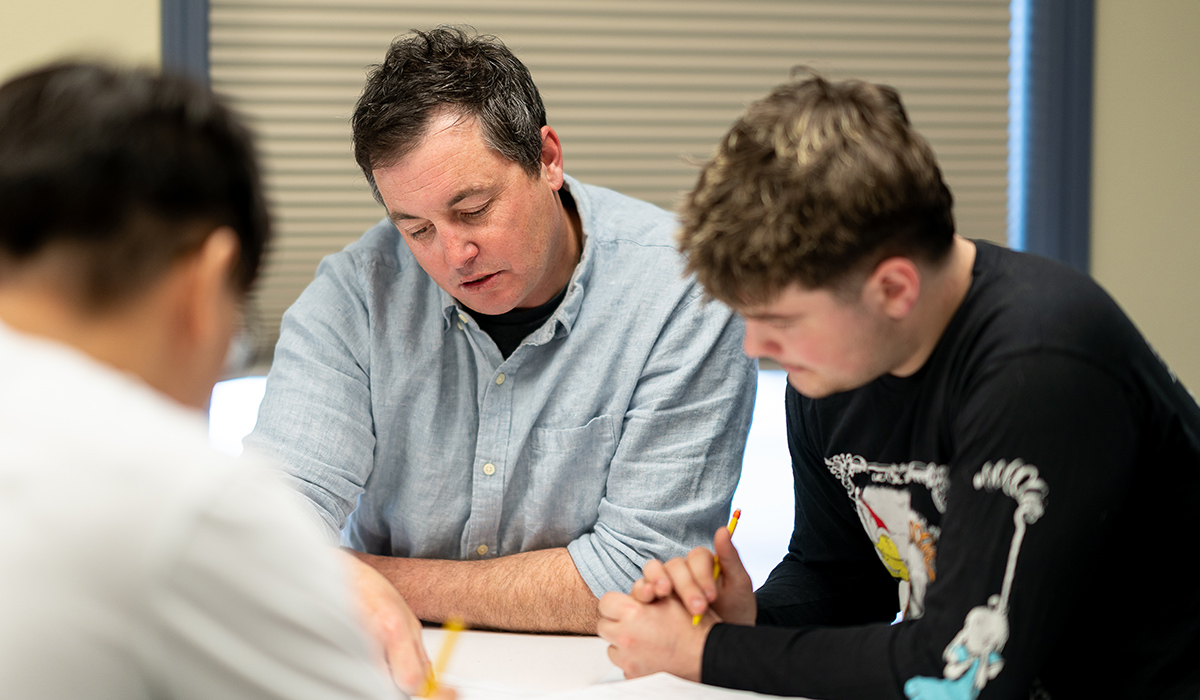 An instructor sits at a table and works with a student on an assignment.