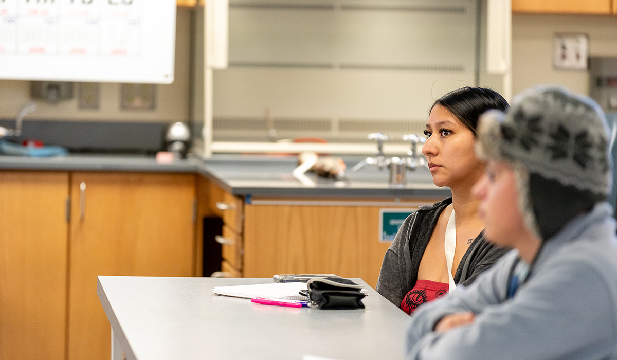 Two students sitting in a lab listen to their instructor.