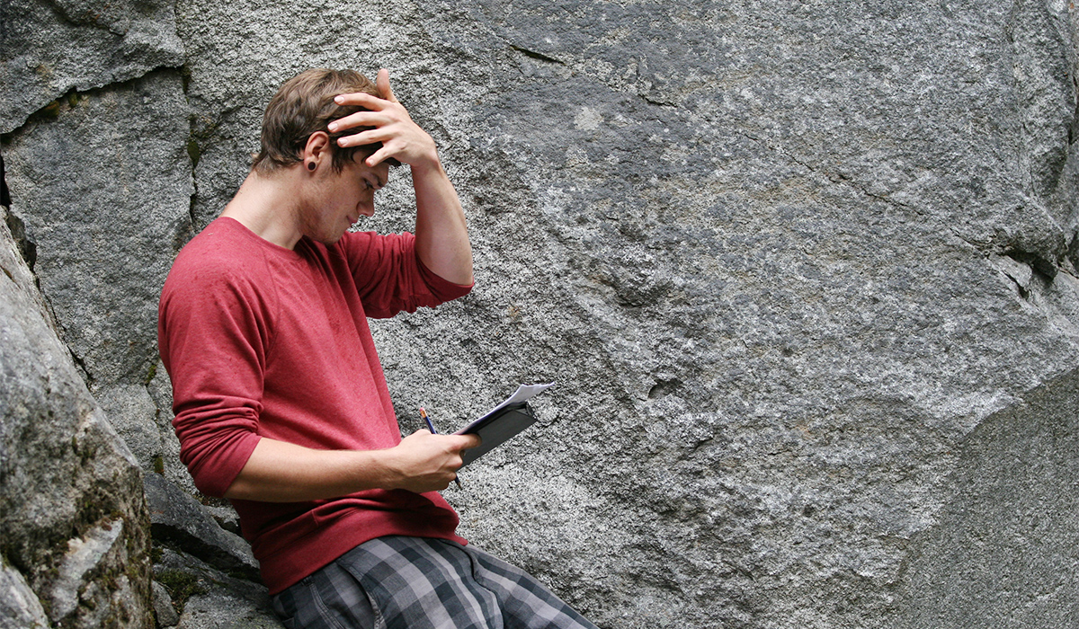 A student holding a journal stands against a rock wall.