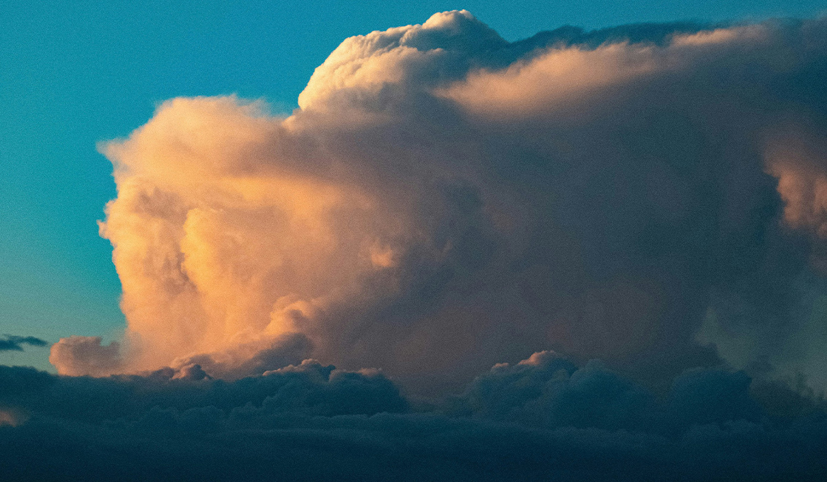 A cumulonimbus cloud turning pink and orange in the sunlight.