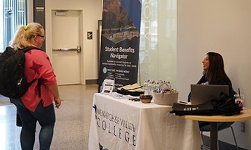 Magali Olguin-Ramos sits at a table and talks with a student who is passing by.
