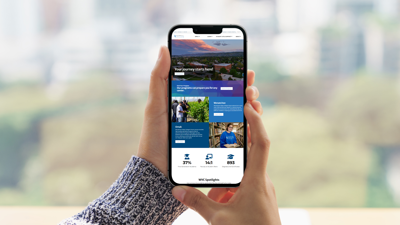 A pair of hands hold a cell phone with an image of the WVC website on it.