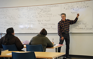 Professor Mike Choman stands beside a whiteboard 