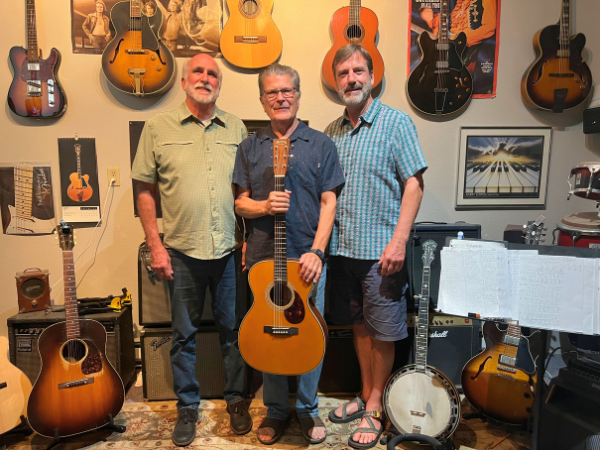 Jack Johnson, Michael Choman, and Derek Sheffield stand together in a room surrounded by guitars.